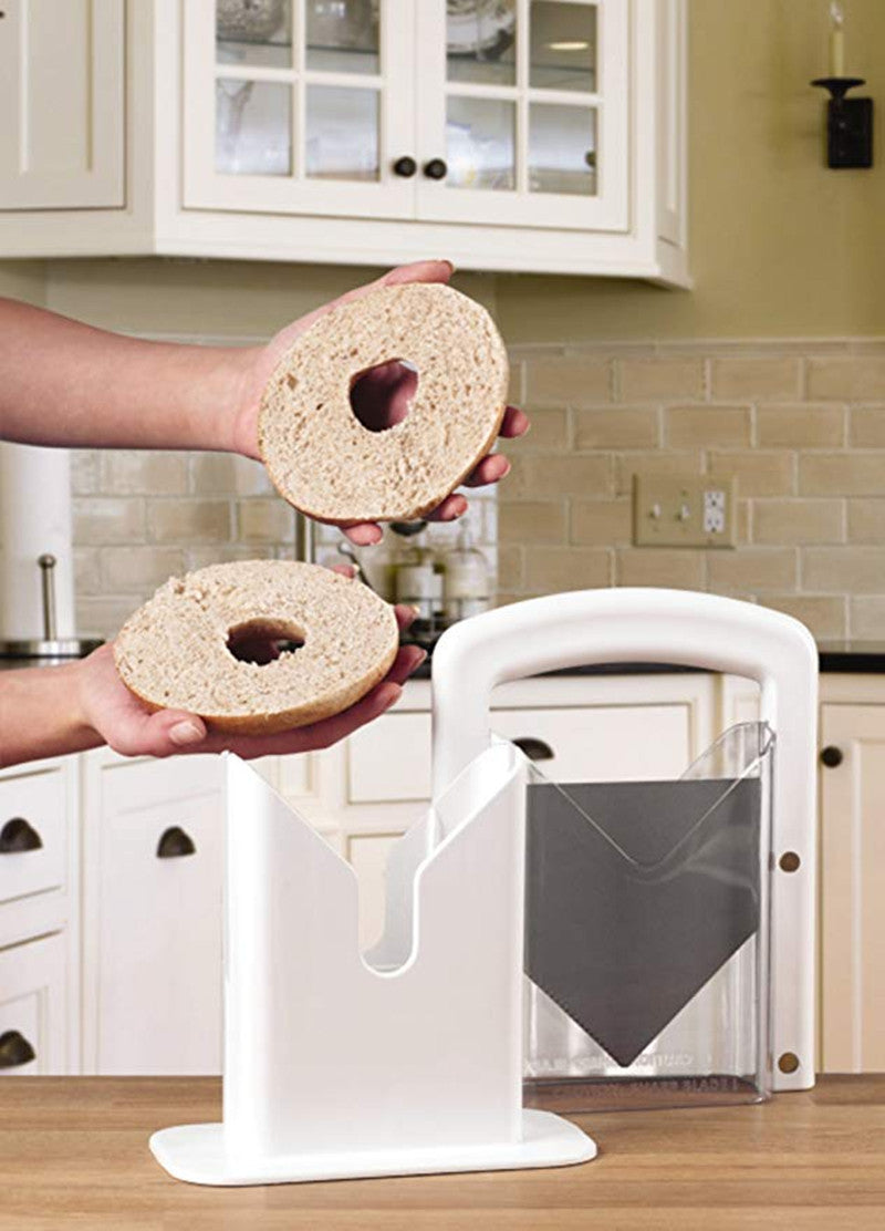 Person holding two bagels above a white bagel slicer in a kitchen.